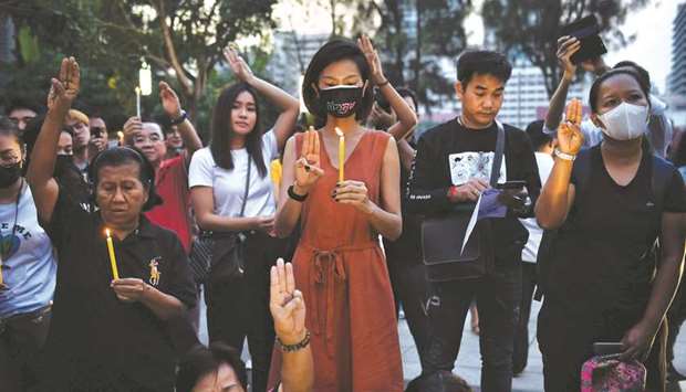 Pro-democracy supporters light candles and show three-fingered Hunger Games salutes, a day after the Constitutional Court ruled to dissolve the progressive opposition Future Forward Party, at Thammasat University in Bangkok, yesterday.