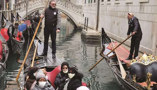 Tourists wearing surgical masks wait for a gondola ride to start in Venice.