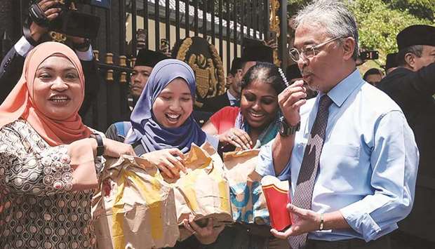 Malaysiau2019s King Sultan Abdullah Sultan Ahmad Shah (right) eats as he hands out packages of fast food to reporters standing outside the National Palace in Kuala Lumpur yesterday. Intense political jockeying is underway to form a new government in Malaysia after Mahathir Mohamed, the worldu2019s oldest leader, resigned then was appointed interim leader.