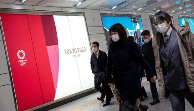 People wearing protective face masks, following an outbreak of the coronavirus, walk past an advertising billboard of Tokyo Olympics 2020, near the Shinjuku station in Tokyo