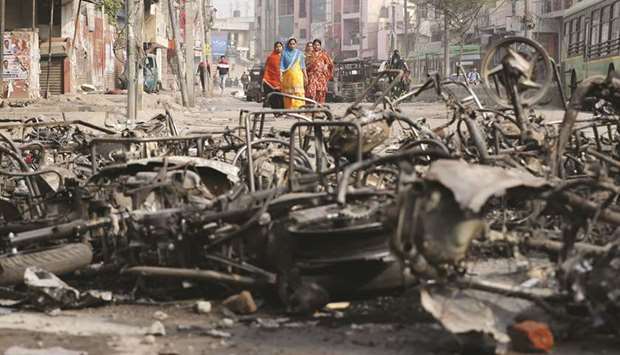 Women walk past charred vehicles in a riot affected area in New Delhi yesterday.