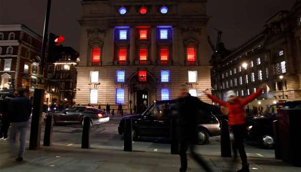 Passers-by pose for a photograph in front of the Department for International Trade, illuminated by red, white and blue lights in central London