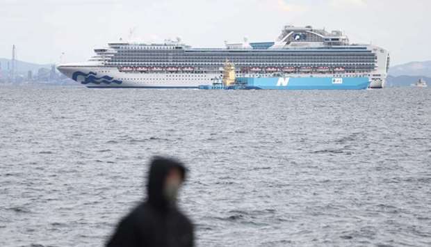 A member of the media (in foreground) looks out toward the Diamond Princess cruise ship (in background) with over 3,000 people as it sits anchored in quarantine off the port of Yokohama