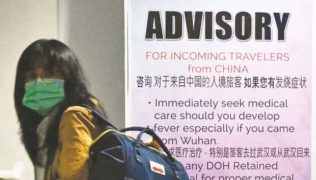 A traveller wearing a protective face mask walks past a travel health advisory sign upon arrival at the international airport in Manila.