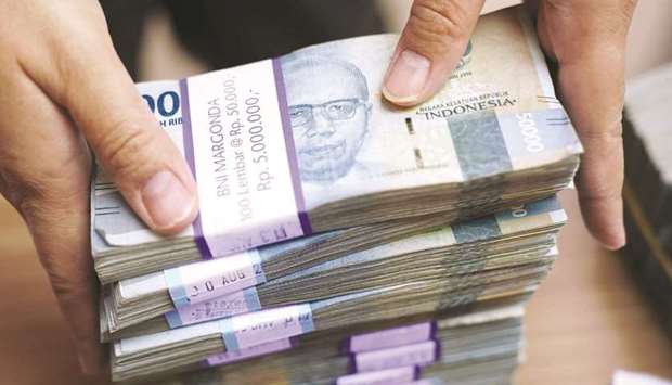 An employee handles Indonesian rupiah banknotes at a currency exchange in Jakarta. A macro hedge fund spun out of Millennium Management is building bullish positions in the Indonesian rupiah and Singapore dollar, betting that measures adopted by the two countries could boost their currencies.