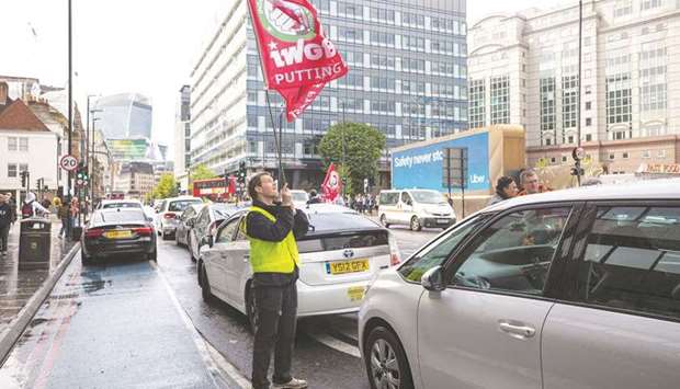 A protesting Uber driver waves a flag near the UK headquarters of Uber Technologies in London on May 8, 2019. The UK Supreme Court yesterday ruled that the service performed by drivers was u201cvery tightly defined and controlled by Uberu201d so they could not be considered to be self-employed.