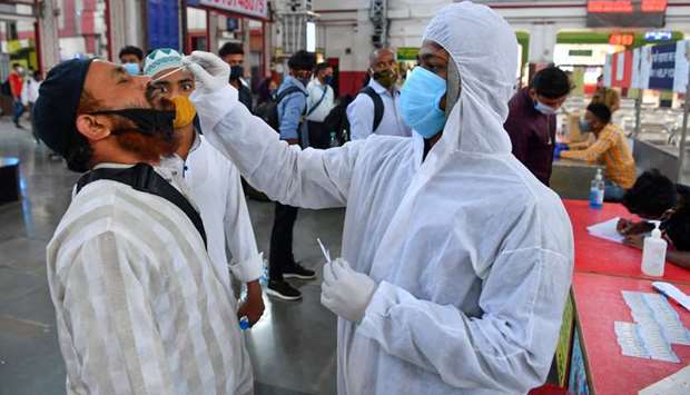 A health worker wearing protective gear takes a nasal swab sample of arriving passengers for conducting RT-PCR Covid-19 coronavirus tests during a screening at a railway terminus in Mumbai