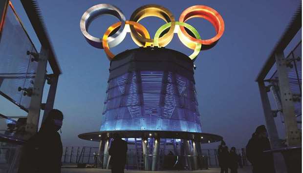 People wearing face masks are seen near the lit-up Olympic rings at top of the Olympic Tower, a year ahead of the opening of the 2022 Winter Olympic Games, in Beijing, China, yesterday. (Reuters)