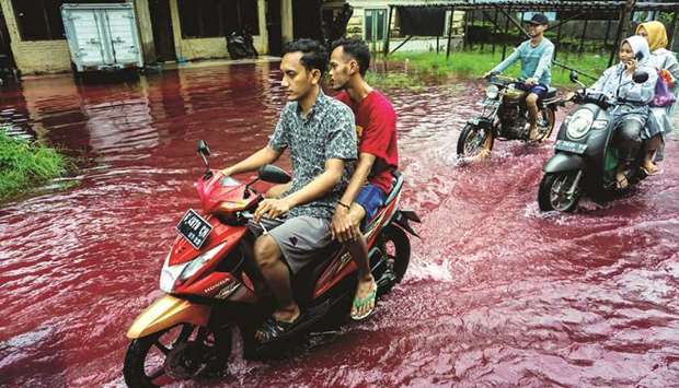 People ride motorbikes through a flooded road with red water due to the dye-waste from cloth factories, in Pekalongan, Central Java province, yesterday.