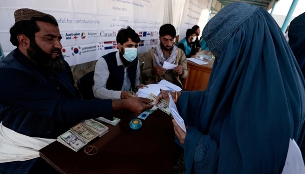 A displaced Afghan woman receives money from an UNHCR worker at a distribution center on the outskirts of Kabul, Afghanistan October 28, 2021. REUTERS