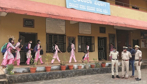 Schoolgirls arrive to attend their classes as police officers stand inside the premises of a government girls school in Udupi town in Karnataka, India, yesterday.