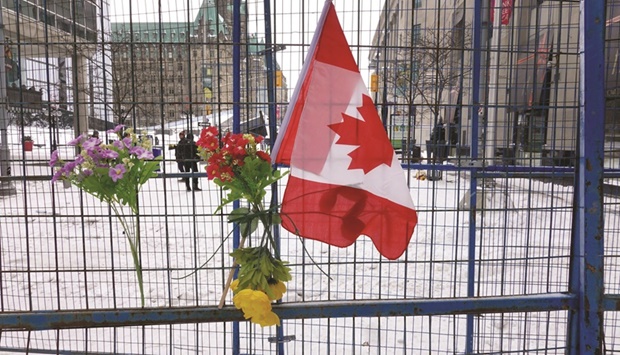 Flowers and a flag hang on a barrier fence near Ottawau2019s Parliament Hill.