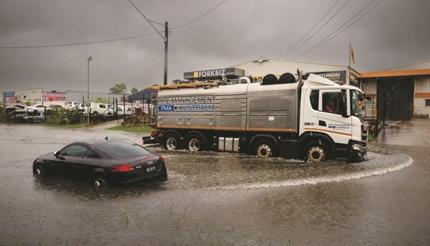 A truck drives past an abandoned car on a flooded road at Rocklea, in Australiau2019s Queensland state.