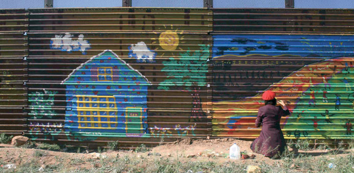 Artist Gretchen Baer paints on a fence marking the US border in Naco, Mexico.