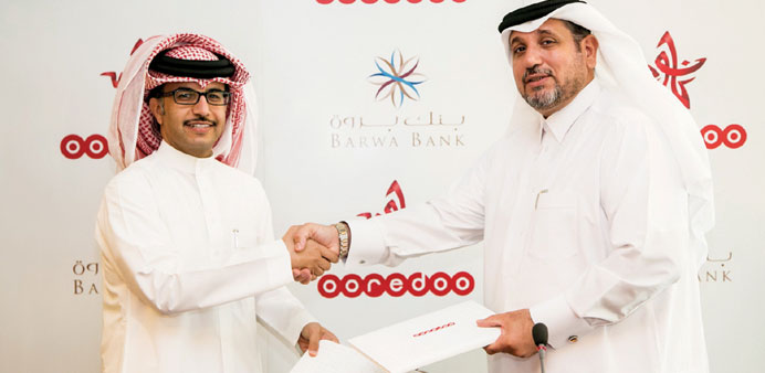 Ooredoo and Barwa Bank officials exchange documents after signing the agreement.