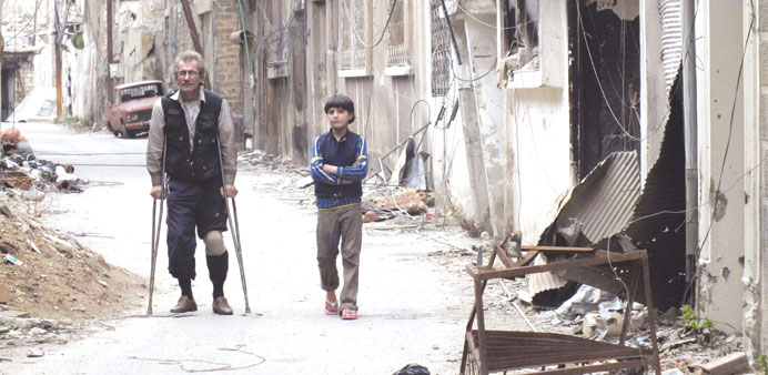 Residents walk by damaged buildings in Homs yesterday. 