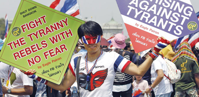 An anti-government protester holds placards during a rally at the Royal Plaza near Government House in Bangkok yesterday.