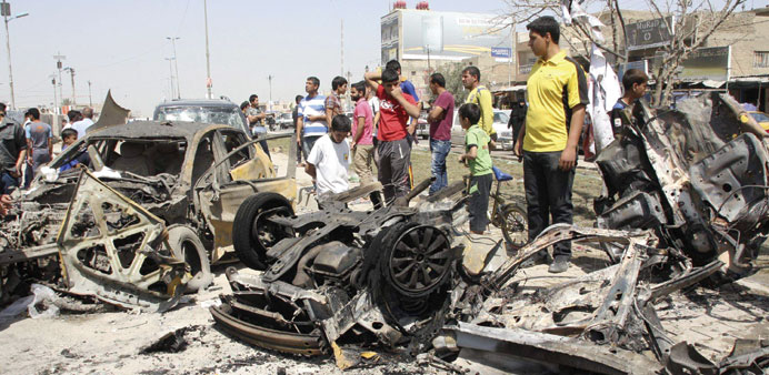 Residents look at wrecked cars at the site of a bomb attack in Sadr City in Baghdad yesterday.