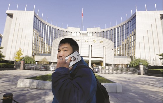 A man talks on his mobile phone while walking past the headquarters of the Peopleu2019s Bank of China in Beijing. The PBoC is trying to keep liquidity flush to support the economy and cushion the pain from structural reforms, but officials have cautioned against excessive loosening that could increase downward pressure on yuan.