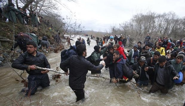 Migrants wade across a river near the Greek-Macedonian border, west of the village of Idomeni, on Monday.