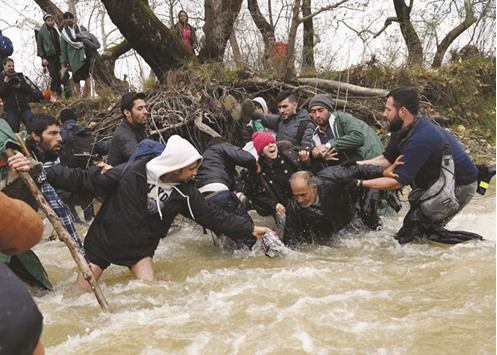 Members of a migrant family fall as they try to cross a river into Macedonia, from a makeshift camp near the Greek village of Idomeni.