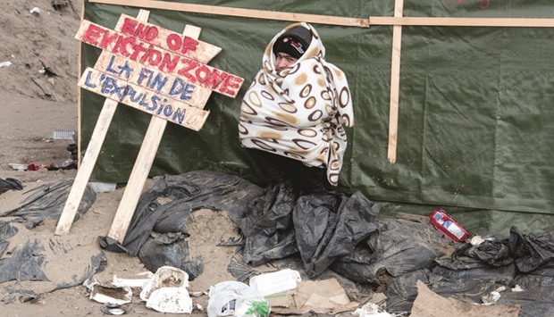 A man sits next to a placard yesterday in the northern part of the so-called u2018Jungleu2019 migrant camp in Calais, during the end of the dismantling of the campu2019s southern part.