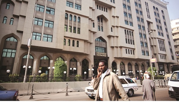 A pedestrian uses his mobile phone as he passes Egyptu2019s central bank in Cairo. Egyptu2019s economic recovery has been slowed by a foreign-currency shortage that has boosted black market demand for dollars.