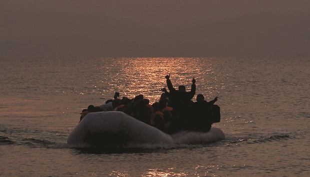 Refugees and migrants wave as they approach the shores of the Greek island of Lesbos on a dinghy during sunrise yesterday.