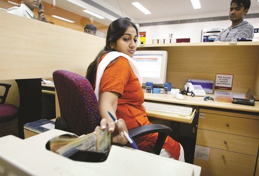A cashier at the ICICI bank branch in New Delhi places rupee notes in a counting machine. Citibank sees the rupee holding in a range as investor appetite for developing-nation securities is pressured by the Federal Reserveu2019s policy tightening and yuan weakness.