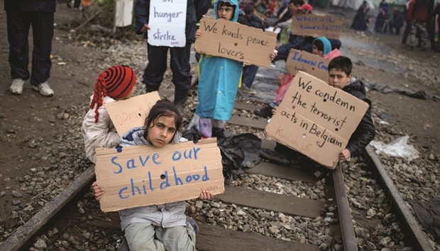 Children hold placards yesterday at a makeshift camp for migrants and refugees at the Greek-Macedonian border near the Greek village of Idomeni. The UN refugee agency has harshly criticised an EU-Turkey deal on curbing the influx of migrants to Greece, saying that reception centres had become u2018detention facilitiesu2019, and suspended some activities in the country.
