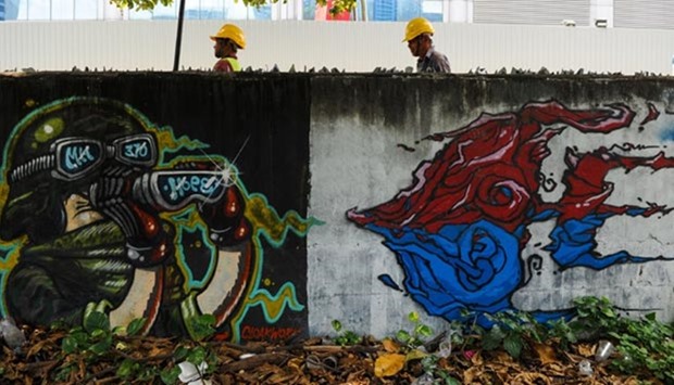 Construction workers walk behind a mural dedicated to missing Malaysia Airlines flight MH370, on a wall next to a parking lot in Kuala Lumpur on Thursday.