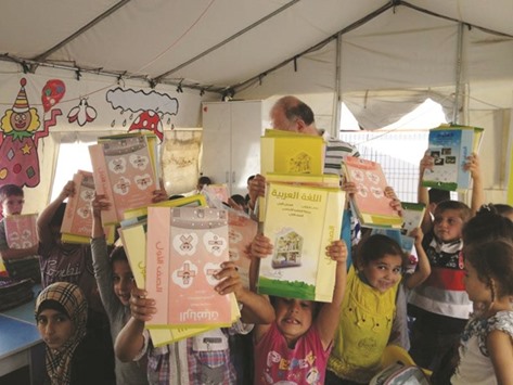 Syrian refugee children hold aloft books provided by Qatar Charity.