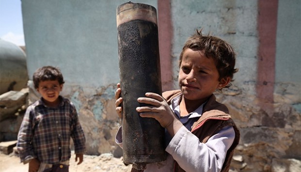 A young boy struggles to hold a large piece of exploded artillery shell following bombing near his home in Sanaa