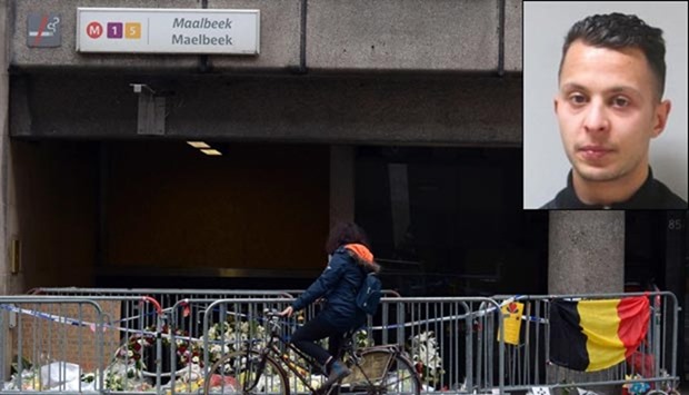 A woman cycles by a makeshift memorial for the victims of last week terror attacks outside the Maalbeek metro station in Brussels on Thursday. Inset, Salah Abdeslam.