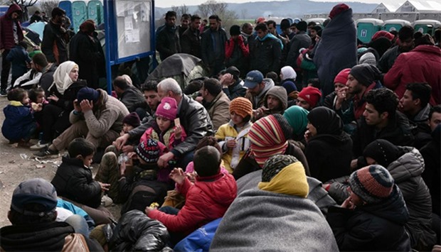 Refugees and migrants sit on the ground as they wait to cross the border