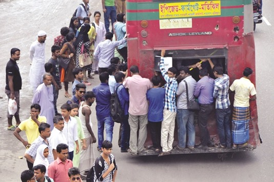 Passengers climb onto an overcrowded public transport vehicle in Dhaka.