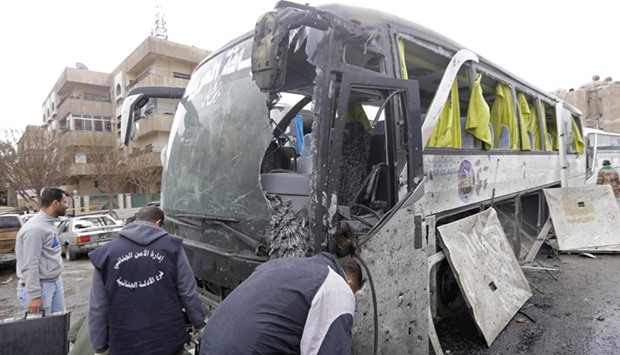 Syrian forensics examine a damaged bus at the scene of a bombing following twin attacks targeting Shia  pilgrims in Damascus' Old City on March