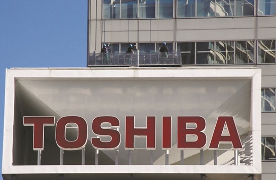 The logo of Toshiba is seen as window cleaners work on the companyu2019s headquarters in Tokyo. The Japanese conglomerate is offering a majority stake in the chip unit and would be willing to sell the entire business, sources said yesterday.