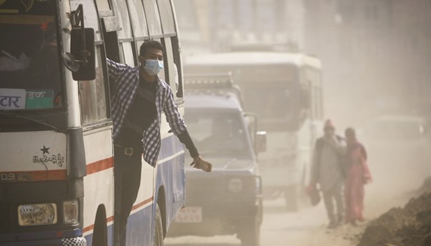A bus conductor wearing a mask hangs onto a bus as he travels through a dusty road in Kathmandu yesterday.