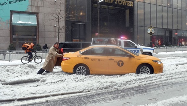 A passenger pushes a cab stuck on a snow and sleet-covered street in New York on Tuesday.