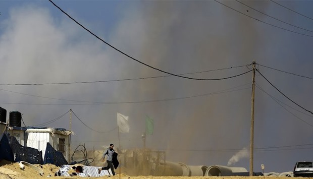 A Palestinian man runs for cover as smoke rises following an Israeli air strike