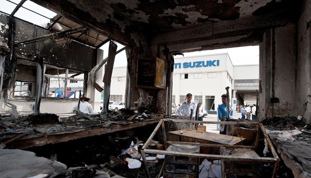 In this photograph taken on July 19, 2012, Indian private security guards look at the burnt reception office at the main gate of the Maruti Suzuki Production Facility in Manesar, about 45 kms from New Delhi.