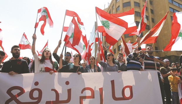 Protesters wave Lebanese national flags during a demonstration against a proposed tax increase, in front of the government palace in Beirut yesterday. The placard reads in Arabic: u201cWe will not pay.u201d