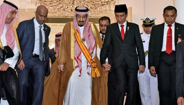 Saudi King Salman holds hand of  Indonesia President Widodo as they leave the presidential palace