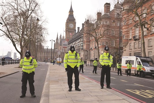 Police officers bow their heads as they stand near a police cordon directly outside New Scotland Yard and within sight of the Houses of Parliament (background) in central London yesterday during a minuteu2019s silence to commemorate the victims of the terror attack at the parliament on Wednesday.