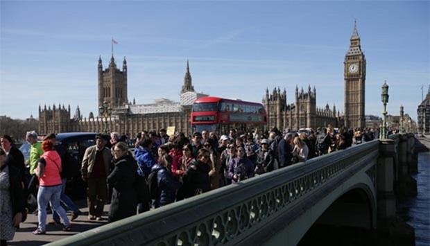 People walk along Westminster Bridge in front of the Houses of Parliament in London on Sunday.