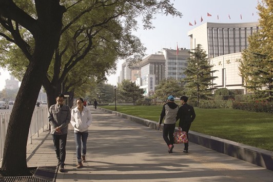Pedestrians walk past the Peopleu2019s Bank of China headquarters (right) in Beijing. PBoC governor Zhou Xiaochuan said the country is preparing to further open its financial  sector and signalled doing so will involve negotiations over how other nations treat Chinese investors.
