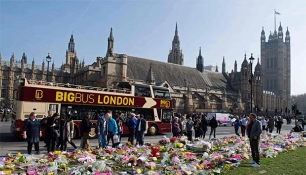 People stop to look at floral tributes to the victims of the March 22 terror attack outside the Houses of Parliament in Westminster, London on Monday.