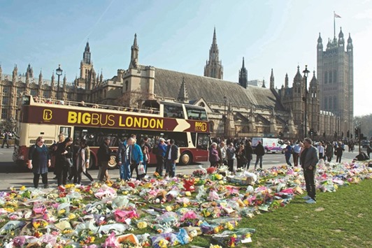 People stop to look at floral tributes to the victims of the March 22 terror attack outside the Houses of Parliament in Westminster, central London, yesterday.