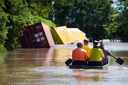 A group of workers paddle in a small boat to check on a flooded house in Beenleigh, Queensland
